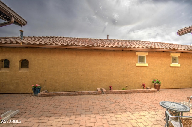 view of side of property with a patio area, a tiled roof, and stucco siding