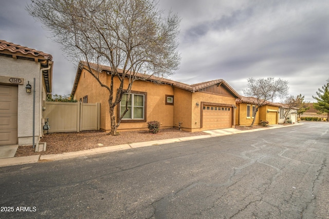 view of front of house featuring a garage, a tile roof, fence, and stucco siding