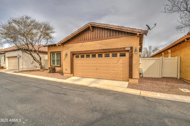 view of front of home featuring a garage, concrete driveway, a tile roof, fence, and stucco siding