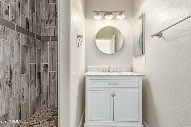 full bathroom featuring a textured wall, a tile shower, and vanity