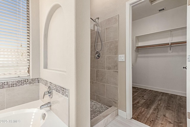 bathroom with visible vents, a garden tub, a walk in closet, a shower stall, and a wealth of natural light