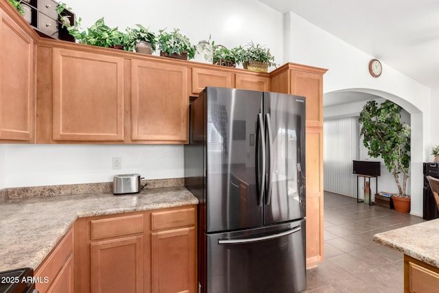 kitchen featuring light tile patterned floors, arched walkways, lofted ceiling, freestanding refrigerator, and light countertops