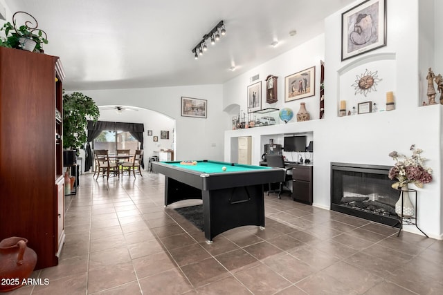 game room featuring arched walkways, a ceiling fan, a glass covered fireplace, vaulted ceiling, and tile patterned flooring