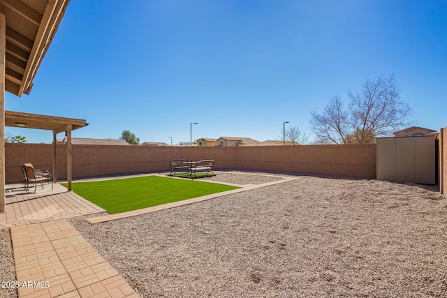 view of yard featuring an outbuilding, a storage unit, a patio area, and a fenced backyard