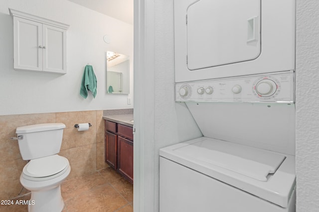 bathroom with vanity, stacked washer / dryer, tile patterned floors, tile walls, and toilet