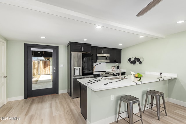 kitchen with appliances with stainless steel finishes, light stone countertops, light hardwood / wood-style floors, kitchen peninsula, and a kitchen bar