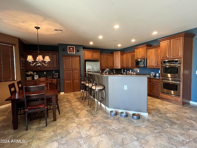 kitchen featuring pendant lighting, a notable chandelier, stainless steel appliances, an island with sink, and a breakfast bar area