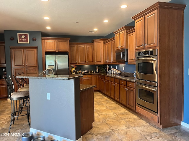 kitchen featuring a breakfast bar area, black appliances, a kitchen island with sink, sink, and dark stone countertops