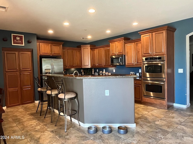 kitchen with a kitchen breakfast bar, stainless steel appliances, dark stone counters, and a kitchen island with sink