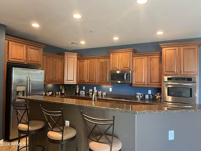 kitchen featuring dark stone counters, a kitchen bar, stainless steel appliances, a kitchen island, and sink