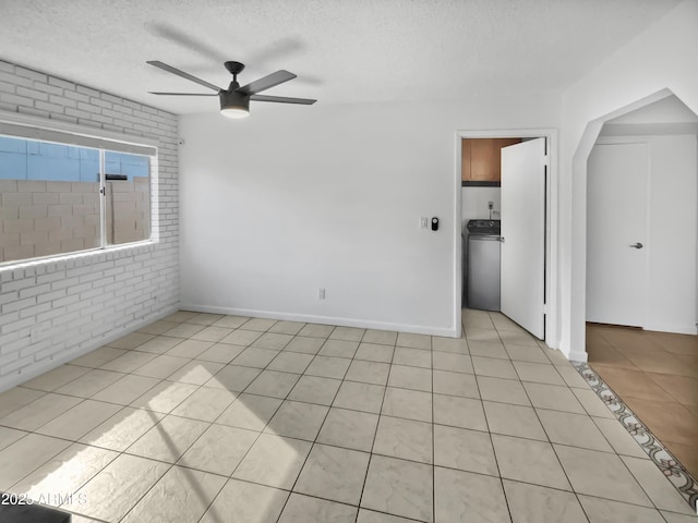 spare room with a textured ceiling, light tile patterned floors, ceiling fan, brick wall, and washer / clothes dryer