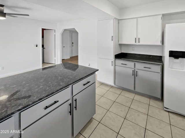 kitchen featuring white cabinetry, light tile patterned floors, white fridge with ice dispenser, ceiling fan, and dark stone counters