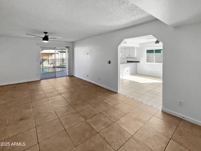 unfurnished living room featuring light tile patterned flooring, brick wall, a textured ceiling, and ceiling fan