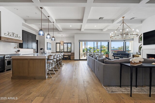 living area with a lit fireplace, beam ceiling, visible vents, and wood finished floors