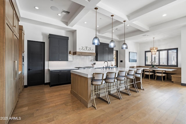 kitchen with decorative light fixtures, light countertops, visible vents, a kitchen island with sink, and wood finished floors