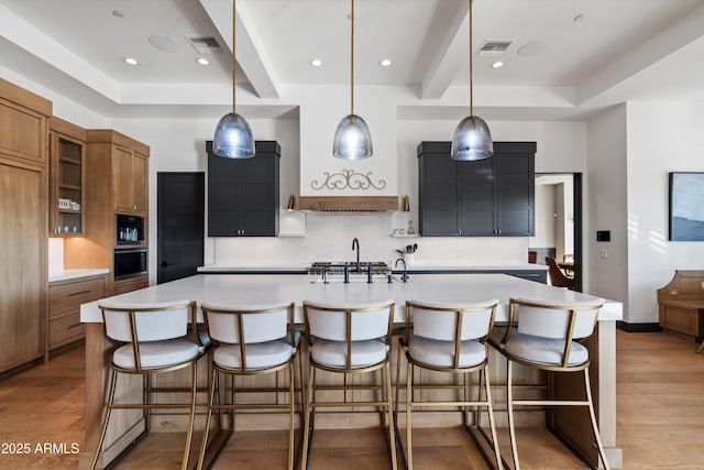 kitchen with brown cabinetry, light wood-style flooring, a spacious island, and light countertops