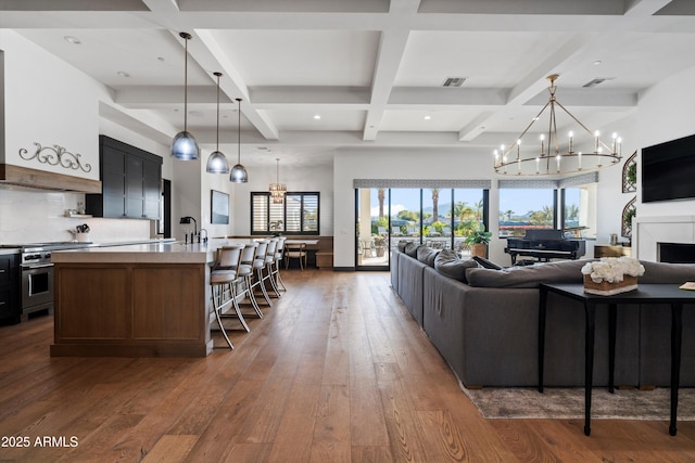 living area featuring a notable chandelier, a fireplace, coffered ceiling, visible vents, and dark wood-style floors