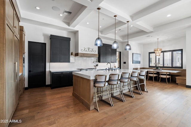 kitchen with wood finished floors, visible vents, light countertops, an island with sink, and decorative light fixtures