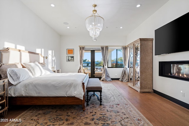 bedroom featuring wood finished floors, a multi sided fireplace, baseboards, access to outside, and french doors