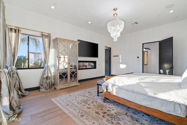 bedroom with a notable chandelier, recessed lighting, visible vents, light wood-style floors, and a glass covered fireplace