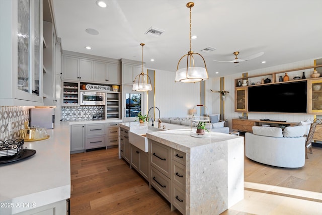 kitchen featuring visible vents, stainless steel microwave, a kitchen island with sink, pendant lighting, and a sink