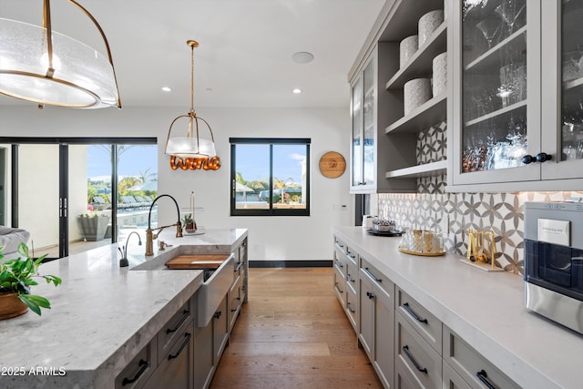 kitchen with decorative light fixtures, open shelves, backsplash, light wood-style floors, and a sink