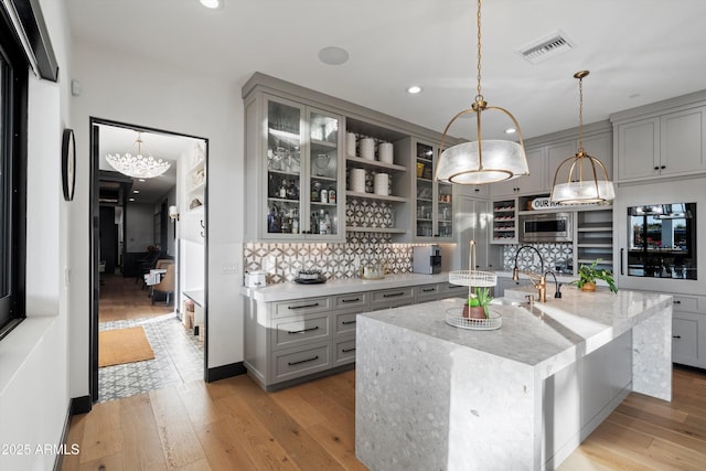 kitchen featuring visible vents, light stone counters, glass insert cabinets, stainless steel microwave, and open shelves