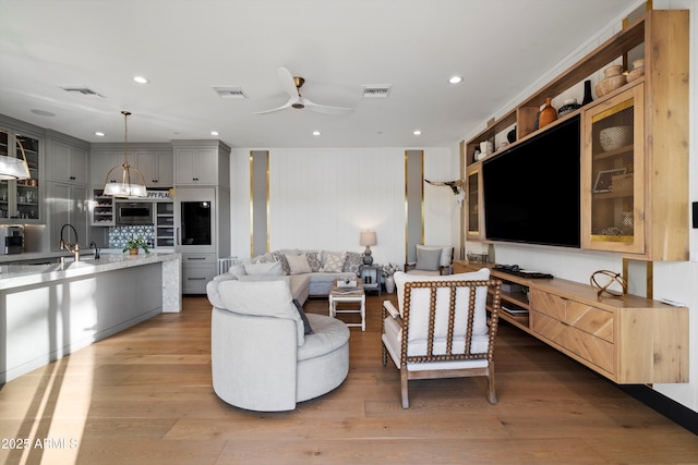 living room with a ceiling fan, visible vents, and wood finished floors