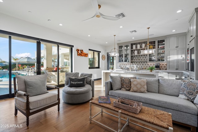 living area featuring ceiling fan, recessed lighting, wood finished floors, visible vents, and wet bar