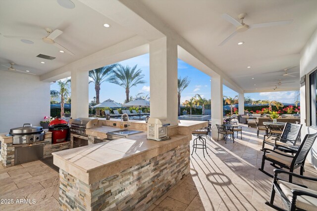 view of patio with grilling area, an outdoor kitchen, a ceiling fan, and outdoor wet bar