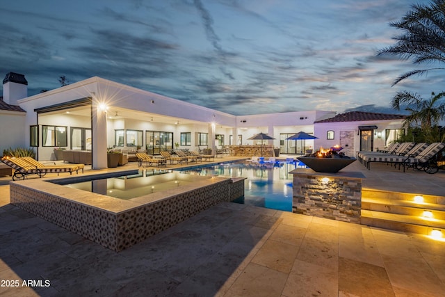 pool at dusk with a hot tub, a patio area, an outdoor living space with a fire pit, and an outdoor pool