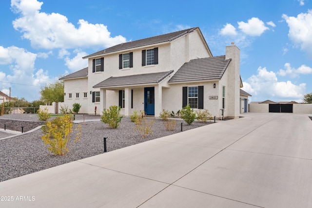 view of front of home with concrete driveway, stucco siding, fence, and a chimney