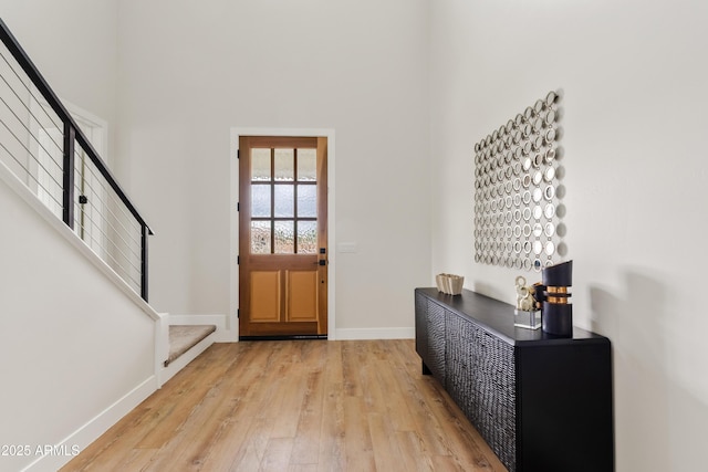 foyer entrance with light wood-type flooring, baseboards, and stairway