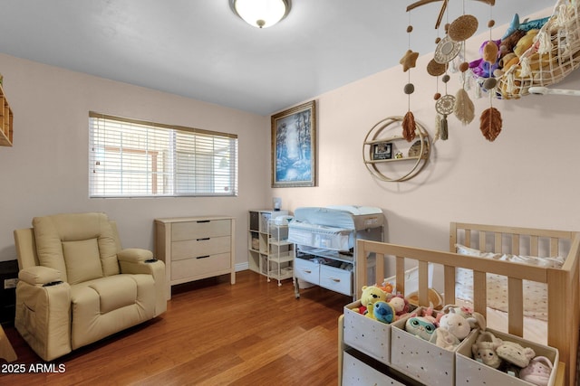bedroom with baseboards, wood finished floors, and a nursery area