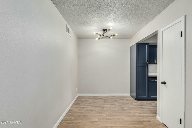 unfurnished room with light hardwood / wood-style floors, a textured ceiling, and a notable chandelier