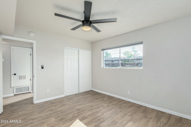 unfurnished bedroom with ceiling fan, a closet, light hardwood / wood-style floors, and a textured ceiling