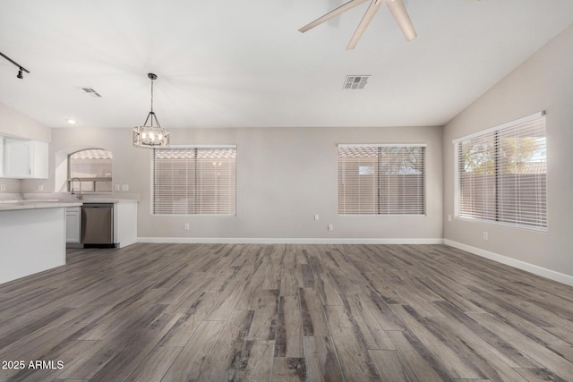 unfurnished living room featuring ceiling fan with notable chandelier, wood finished floors, visible vents, baseboards, and vaulted ceiling