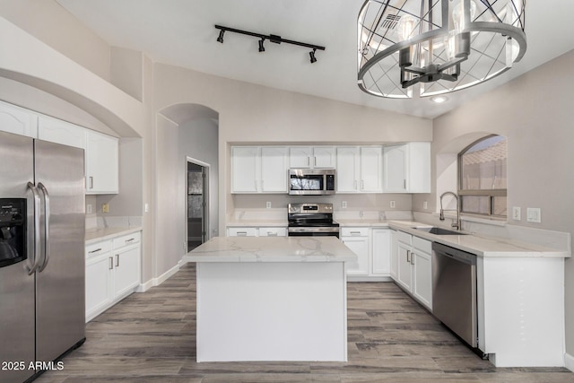 kitchen with appliances with stainless steel finishes, light stone counters, a sink, and a center island