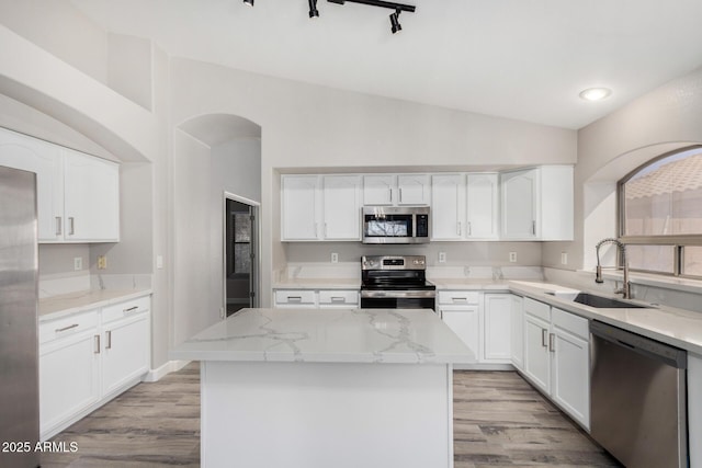 kitchen with light stone counters, stainless steel appliances, a sink, white cabinetry, and vaulted ceiling