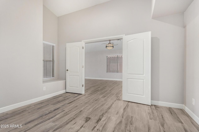 spare room with a towering ceiling, baseboards, and wood finished floors