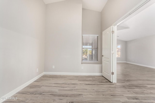 empty room with baseboards, vaulted ceiling, and wood finished floors