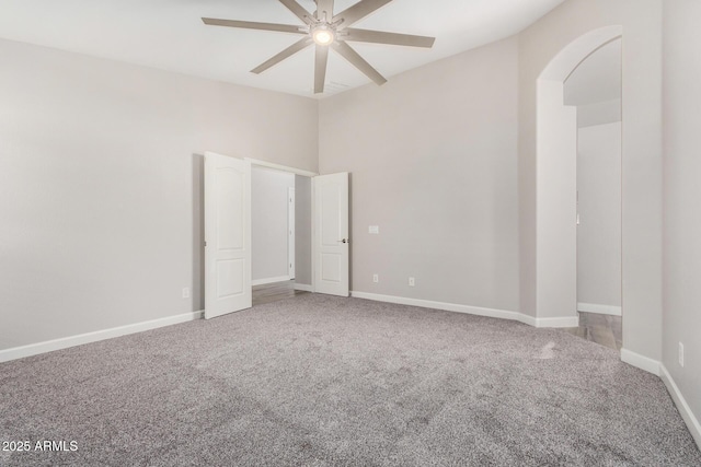 carpeted empty room featuring baseboards, arched walkways, and a ceiling fan