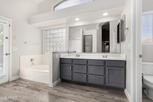 full bathroom featuring a garden tub, toilet, a sink, wood finished floors, and double vanity