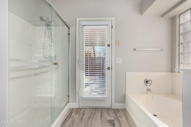 bathroom featuring a garden tub, a stall shower, wood finished floors, and baseboards