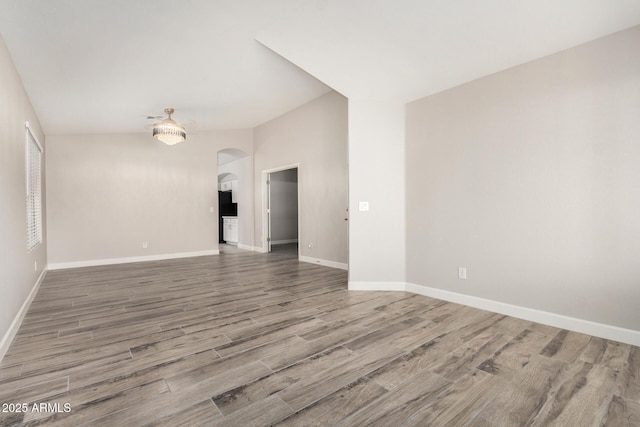 spare room with baseboards, arched walkways, and wood finished floors