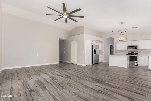 unfurnished living room with arched walkways, ceiling fan with notable chandelier, wood finished floors, baseboards, and vaulted ceiling