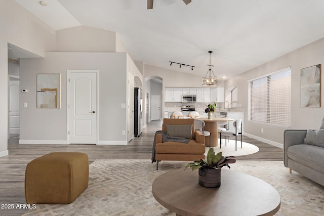 living room with lofted ceiling, light wood-type flooring, arched walkways, and baseboards