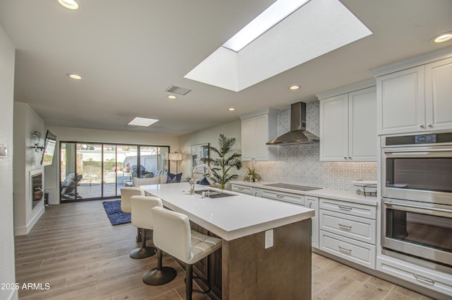 kitchen with double oven, sink, white cabinets, wall chimney range hood, and black electric cooktop