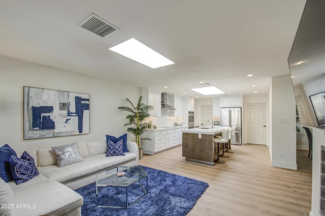 living room featuring a skylight, light hardwood / wood-style floors, and sink