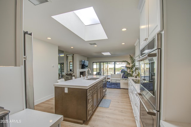 kitchen featuring sink, a skylight, light hardwood / wood-style floors, white cabinets, and a center island with sink